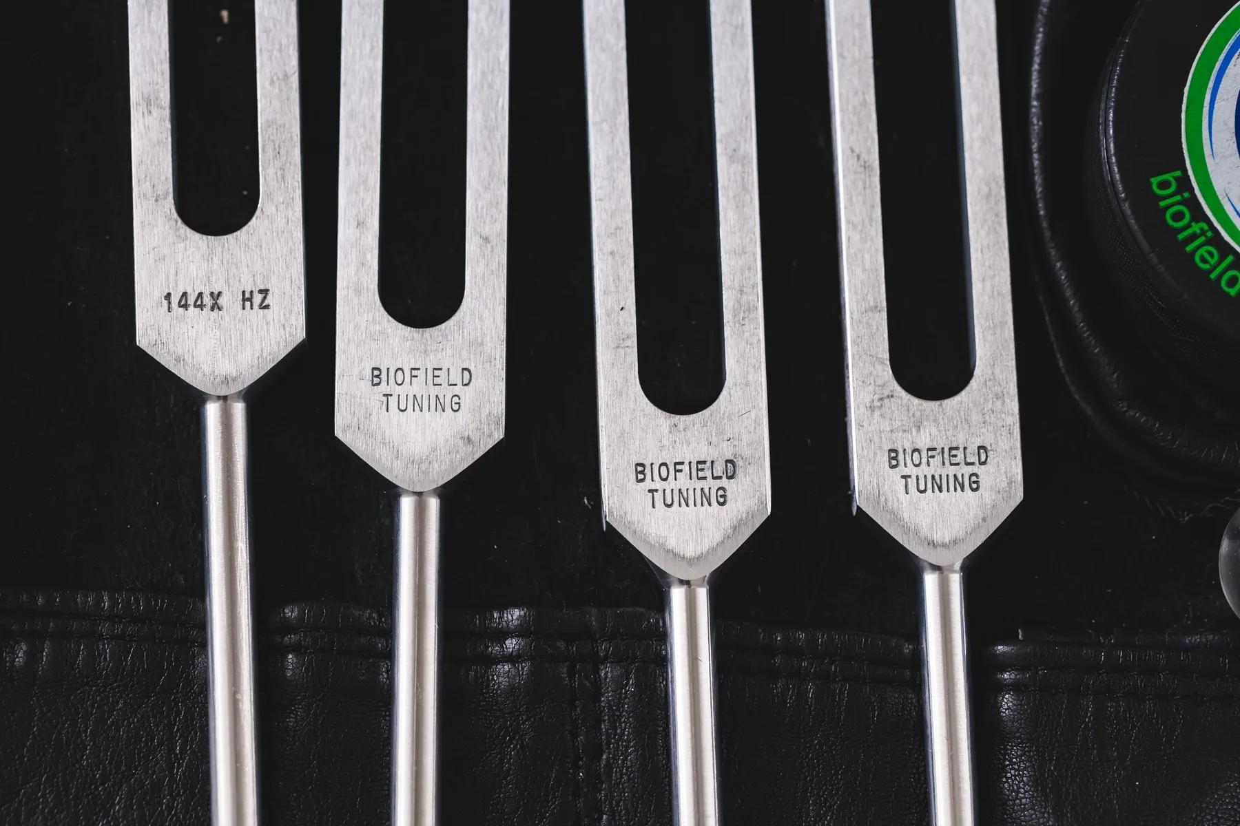 Four Biofield Tuning forks in a row on black leather, engraved with their frequencies