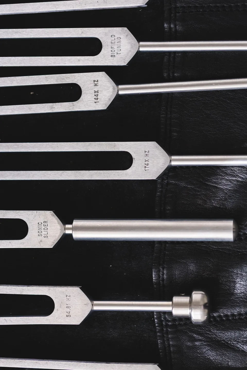 Unweighted forks above a weighted Schumann fork and a Sonic Slider, on black leather