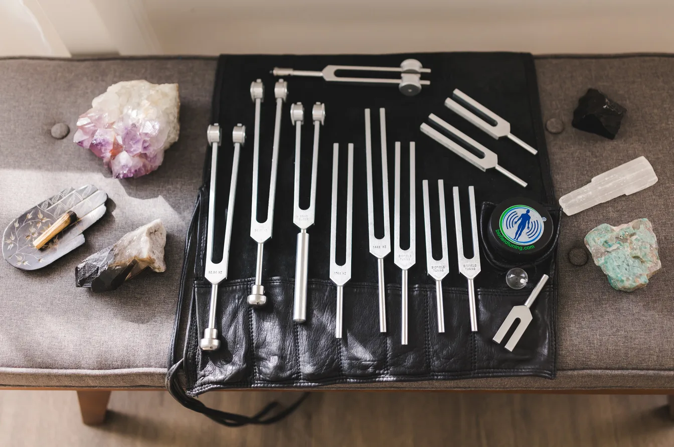 Full set of calibrated Biofield Tuning forks laid out in a leather roll case alongside crystals — practitioner tools used in one-on-one sessions