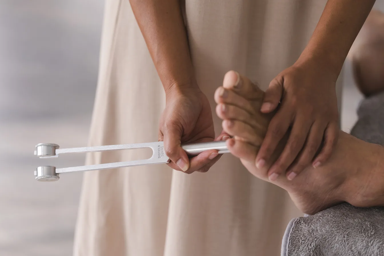 Close-up of Vanessa Fernandez holding a calibrated biofield tuning fork at a client's foot during a one-on-one session