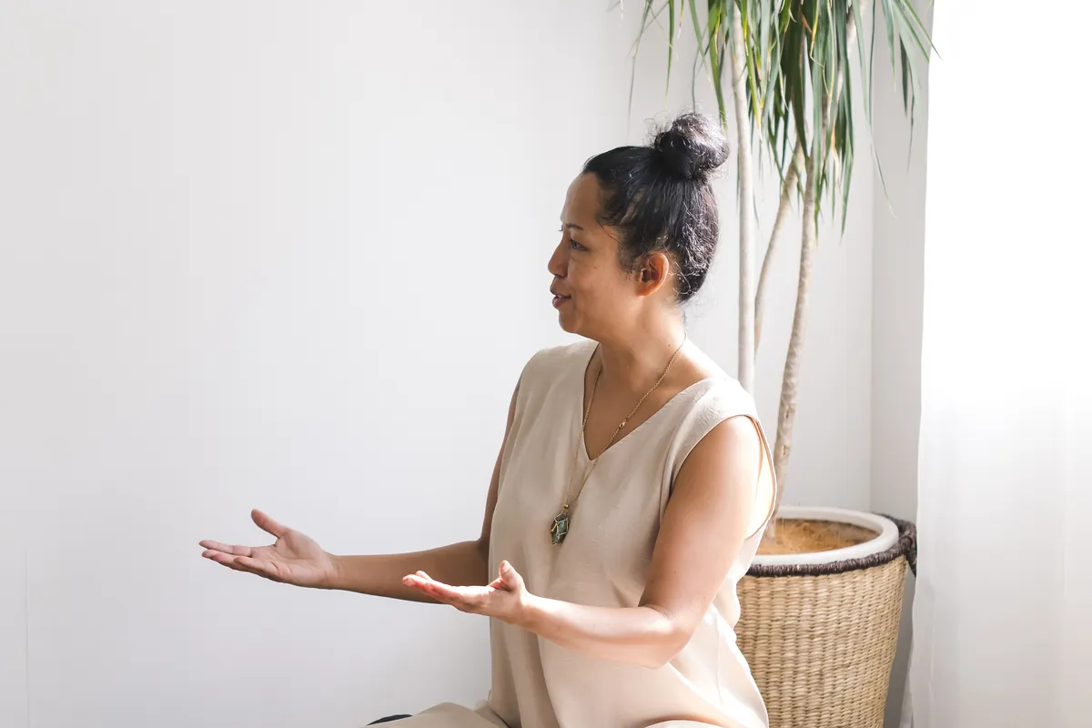 Vanessa Fernandez sitting on a floor cushion, hands open, in a quiet light-filled room