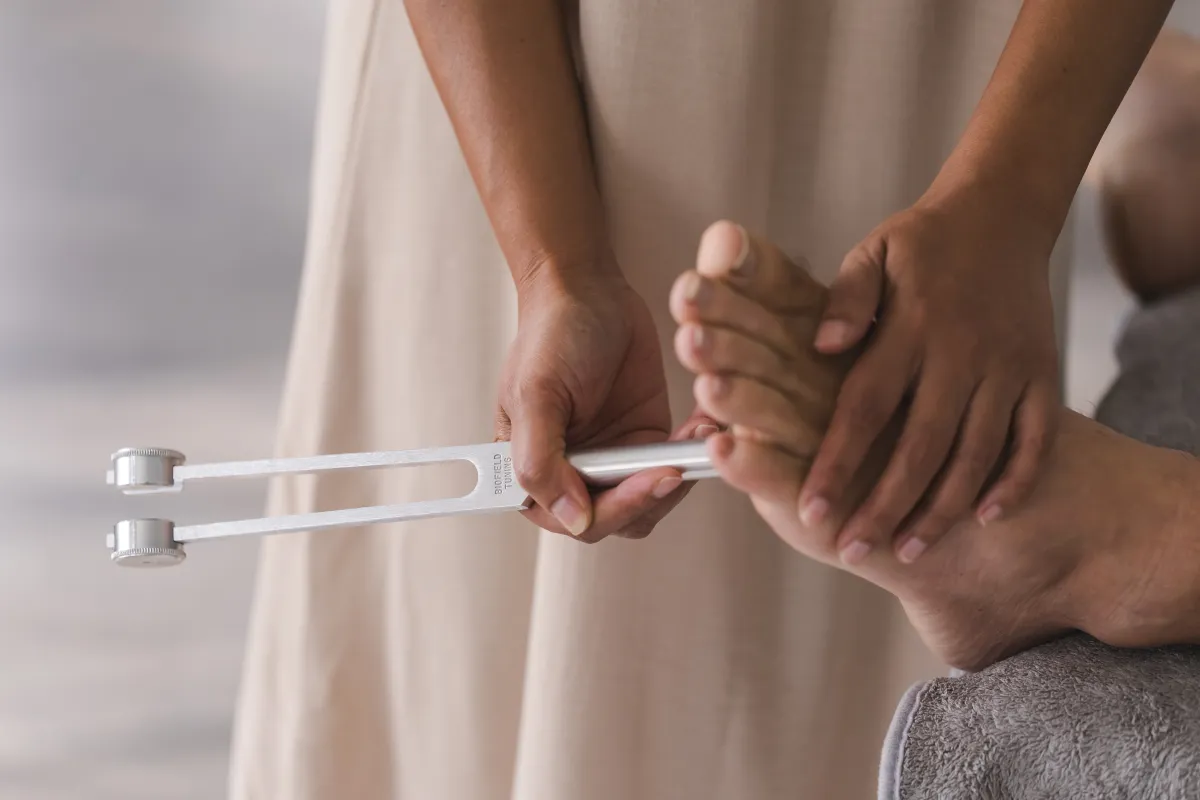 Close-up of Vanessa Fernandez holding a calibrated biofield tuning fork at a client's foot during a one-on-one session